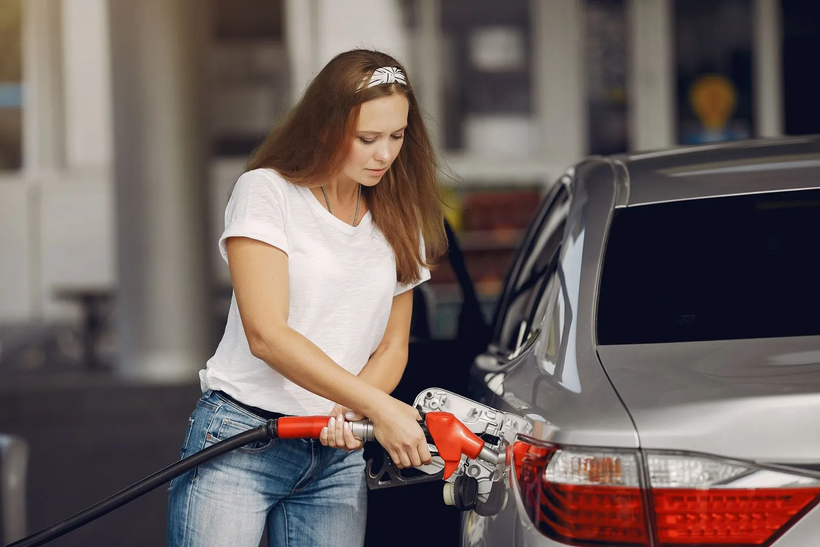 Une conductrice remplit le réservoir de sa voiture, pistolet de carburant en main, dans une station-service
